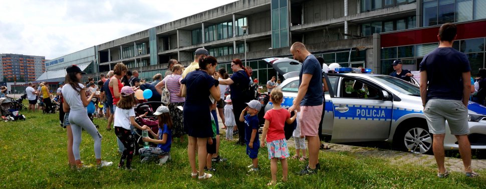 Na zdjęciu widoczny radiowóz za nim policjant i wokół sporo osób, wszyscy uczestniczą w festynie 