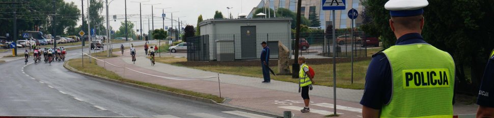 Na zdjęciu widoczny policjant w żółtej kamizelce, z przodu widać jaących drogą kolarzy. 