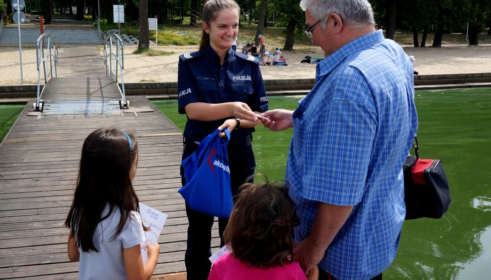 Policjantka daje mężczyźnie breloczek, obok stoi dwójka dzieci.