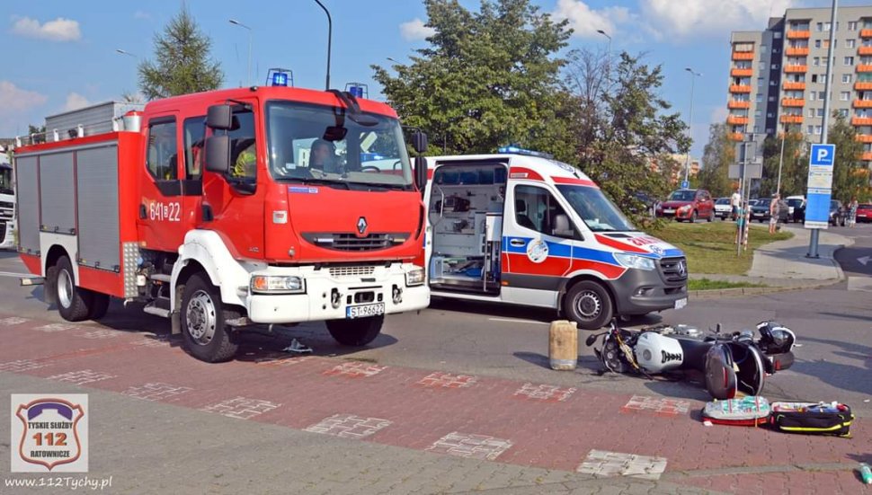 Widoczny wóz straży pożarnej, pogotowie oraz leżący na jezdni przewrócony motocykl.