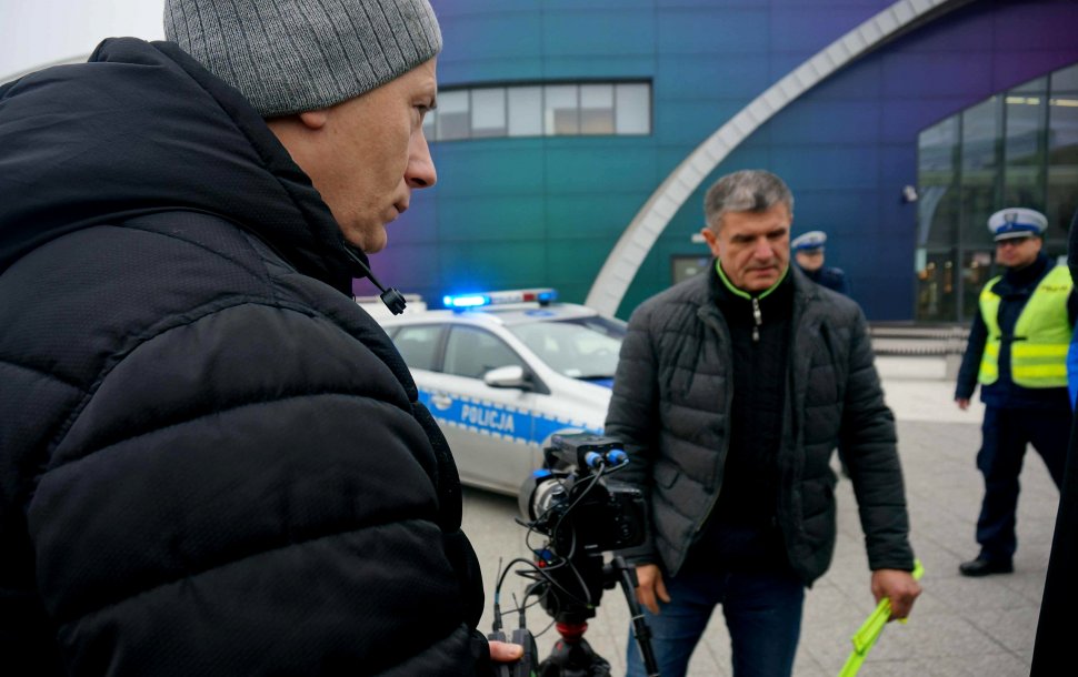 Na zdjęciu widoczni mężczyźni w kurtkach, w tle widać umundurowanego policjanta oraz radiowóz. 