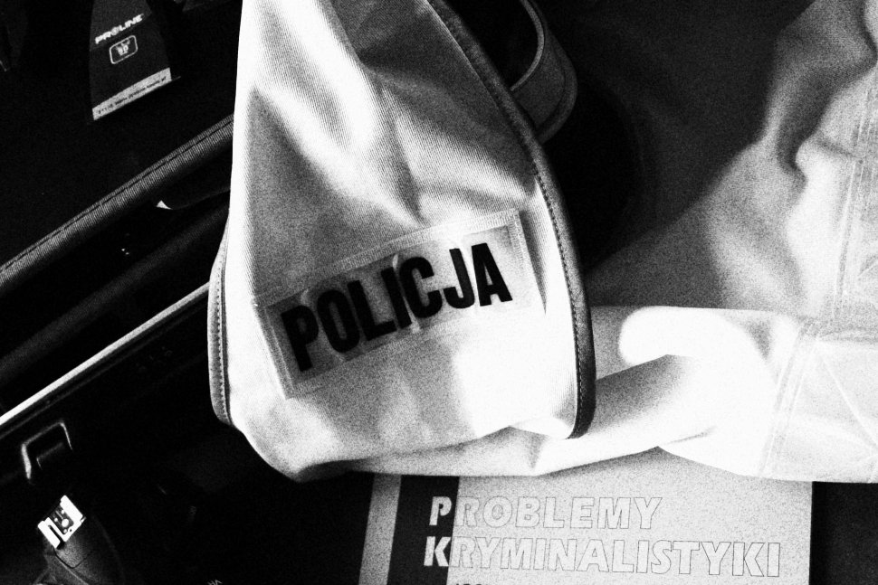 Na zdjęciu widoczny napis "POLICJA" na żółtej kamizelce odblaskowej oraz książka z zagadnieniami dotyczącymi techniki kryminalistycznej.