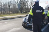 Na obrazku znajduje się stojący tyłem policjant, który zatrzymał do kontroli samochód