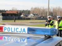 Obrazek przedstawia widoczny z radiowozu napis POLICJA, za nim dwóch policjantów mierzących prędkość