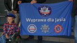 Na obrazku widoczny chłopczyk na wózku trzymający flagę z napisem WYPRAWA dla JASIA