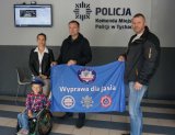 Zdjęcie przedstawia jasia-chłopczyka na wózku oraz jego mamę, a także dwóch policjantów z Tychów, którzy organizują dla Jasia charytatywną wyprawę. Wszyscy trzymają flagę z napisem Wyprawa dla Jasia