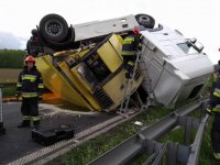 Obrazek przedstawia samochód ciężarowy z żółta naczepą, który dachował i blokuje jezdnię