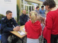 Obrazek przedstawia siedzących przy stoisku profilaktycznym umundurowanych policjantów -dzielnicowych oraz osoby stojące przodem do policjantów i rozmawiające z nimi