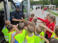 Na obrazku widoczny umundurowany policjant, który rozdaje dzieciom opaski odblaskowe.