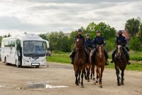 Na obrazku widocznych czterech policjantów na koniach, po lewej stronie autobus stojący na parkingu