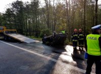 Obrazek przedstawia od prawej: policjanta, dwóch strażaków, wrak samochodu po wypadku oraz lawetę