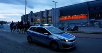 Obrazek przedstawia czterech policjantów na koniach, w tle stadion miejski oraz oznakowany radiowóz