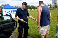 Na zdjęciu policjant na festynie rozdaje opaski odblaskowe, widoczne inne osoby