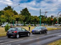 Na zdjęciu widoczny policjant wydziału ruchu drogowego, na jezdni zatrzymane dwa samochody, wszyscy stoją w rejonie skrzyżowania.