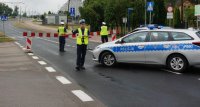 Na zdjęciu widoczny radiowóz oraz policjanci zabezpieczający wyścig kolarski, jeden z nich kieruje ruchem.