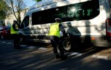 Dwóch policjantów stoi wokół busa, jeden nachyla się nad kołem, sprawdzają stan techniczny busa.