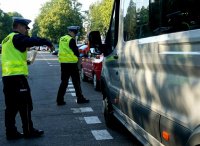 Dwóch policjantów soi obok busa i przygląda się oponom sprawdzając stan techniczny pojazdu.