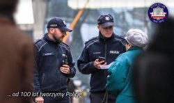 Na zdjęciu widocznych dwóch umundurowanych policjantów rozmawiających ze stojących przy nich osobami.