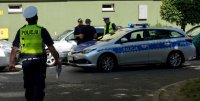 Na parkingu stoi radiowóz, widoczni policjanci oraz funkcjonariusz straży miejskiej, rozmawiają z mężczyzną.