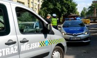 Na zdjęciu widoczny radiowóz Straży Miejskiej, dale Policji, obok stoi policjant, rozmawia z mężczyzną.