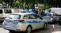 Na zdjęciu widoczne dwa radiowozy policji i jeden straży miejskiej, dalej widoczni policjanci.