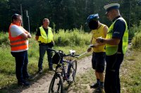 Policjant, pracownik PLK oraz funkcjonariusz SOK rozmawiają z rowerzystą, w tle tory kolejowe.