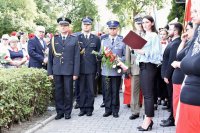 Komendant Miejski Policji insp. Andrzej Trzciński, trzymający kwiaty, stoi w obecności innych mundurowych oraz osób postronnych, podczas uroczystości obchodów 100. rocznicy wybuchu I powstania śląskiego.