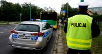 Na zdjęciu widoczny stojący tyłem policjant drogówki w żółtej kamizelce, obok niego radiowóz a przed radiowozem autobus.