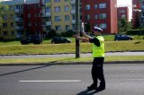 Policjant w żółtej kamizelce stoi na drodze i zatrzymuje &quot;LIZAKIEM&quot; samochód.