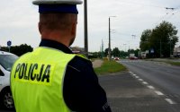 Na zdjęciu widoczny policjant wydziału ruchu drogowego w kamizelce odblaskowej stoi tyłem na drodze.