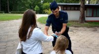 Policjant rozdaje opaski odblaskowe dwóm dziewczynkom.