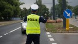 Policjant z ruchu drogowego w odblaskowej kamizelce wskazuje nadjeżdżającemu pojazdowi drogę.