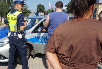 Na zdjęciu widoczny policjant, który pokazuje radiowóz dzieciom oraz ich rodzicom.