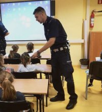 Policjant wydziału  ruchu drogowego rozdaje kolorowanki dla dzieci.