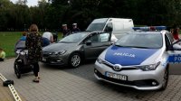 Na zdjęciu widoczne nieoznakowane pojazdy służbowe oraz oznakowany radiowóz, dwóch policjantów z wydziału ruchu drogowego oraz osoby postronne w tym kobieta z wózkiem.