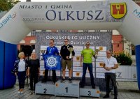 Na podium widoczni funkcjonariusze po cywilnemu, trzymający puchary, obok stoją inne osoby, nad nimi napis: &quot;Miasto i Gmina Olkusz&quot;