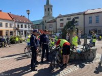 Dwóch policjnatów z wydziału ruchu drogowego rozmawia z rowerzystą, który nachyla się nad rowerem.