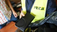 Na zdjęciu widoczna policjanta w kamizelce odblaskowej, która trzyma torebkę z podrobionymi znakami towarowymi.