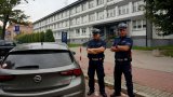 Na zdjęciu widocznych dwóch policjantów drogówki z grupy SPEED, którzy stoją przy nieoznakowanym radiowozie, w tle budynek Komendy Miejskiej Policji w Tychach.