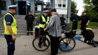 Policjantka z drogówki przekazuje rowerzyście odblask, obok stoi drugi policjant, a za nimi strażacy.