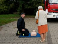 Strażak klęczy obok manekina  i rozmawia ze starszą panią.