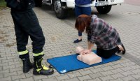 Kobieta ćwiczy udzielanie pierwszej pomocy na manekinie obok stoi strażak.