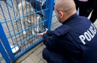 Na zdjęciu widoczny umundurowany policjant, który kuca przy kojcu z psem i wyciąga do niego ręce.