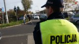 umundurowany policjant ubrany w kamizelkę odblaskową z napisem na plecach POLICJA

w tle widać osoby przemieszczające się w rejonie cmentarza