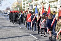 zdjęcie przedstawia uczestników obchodów Święta Niepodległości w Tychach. Przemarsz ulicami miasta, widoczne są sztandary. korowodowi przewodzi oznakowany radiowóz policyjny