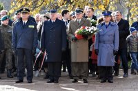 przedstawiciele służb mundurowych w umundurowaniu galowym stoją i oczekują na złożenie kwiatów przed pomnikiem, przedstawiciel WKU trzyma w ręce biało-czerwone kwiaty