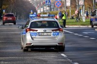 oznakowany radiowóz policji jest na pierwszym planie, przemieszcza się ulicą z prawej strony w tle widać radiowóz straży miejskiej oraz strażnika miejskiego