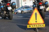 na pierwszym planie jest znak żółty trójkąt z czarnym wykrzyknikiem i napisem WYPADEK
w tle widać dwa motocykle policyjne oraz oznakowany radiowóz policyjny
wszystko stoi na czarnej asfaltowej drodze