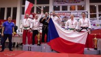 Na zdjęciu widoczne podium, na którym stoją mężczyźni po dwóch na każde z miejsc na podium. Po lewej stronie zdjęcia, na drugim miejscu widoczni Polacy, jeden z nich trzyma uniesioną w górę flagę Polski.