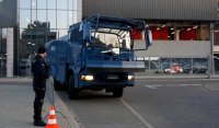 Na zdjęciu widoczny jest umundurowany policjant i pojazd armatki wodnej na tle stadionu miejskiego.